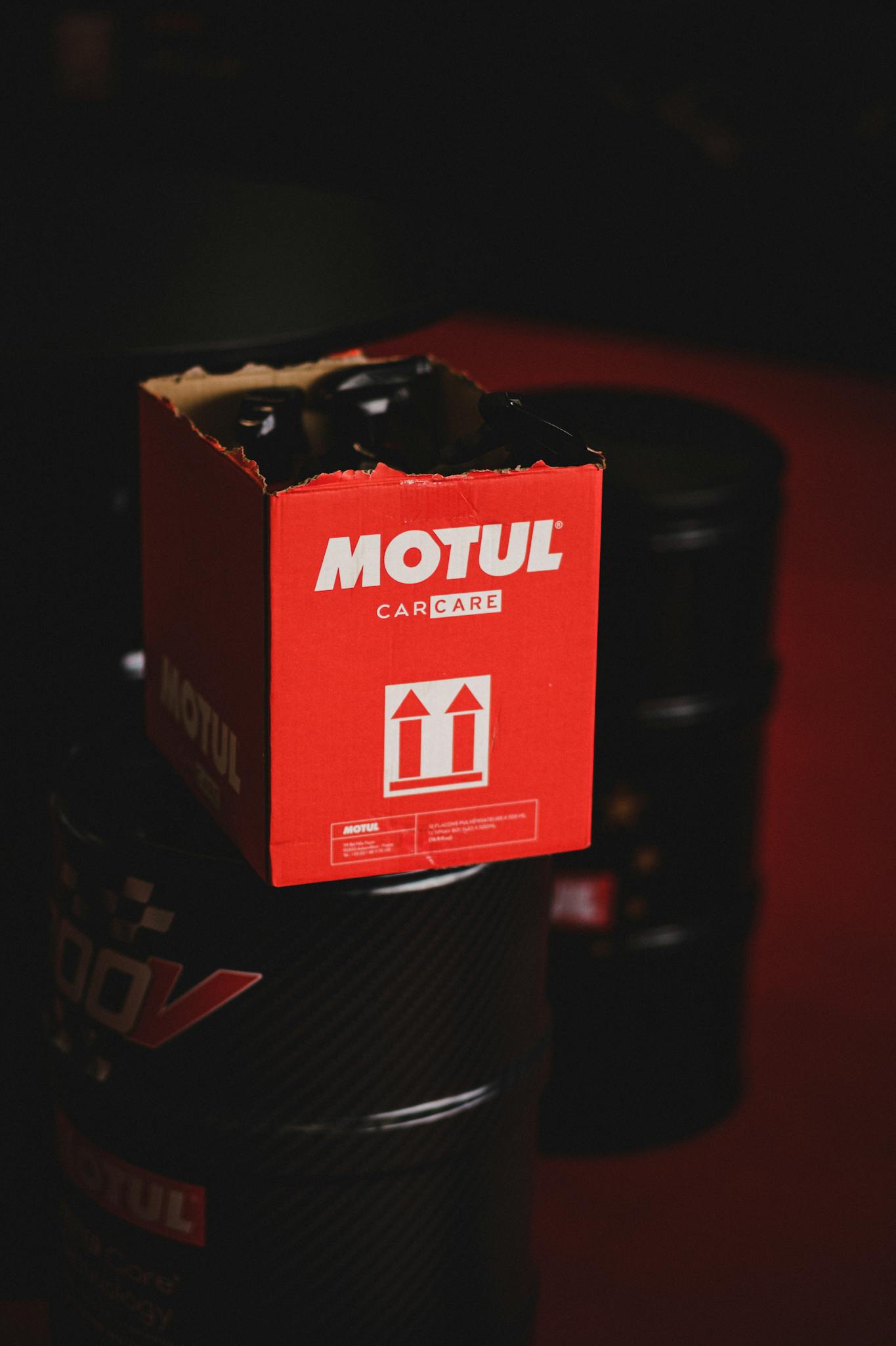 Close-up of Motul car care packaging atop oil barrels in a dark setting.